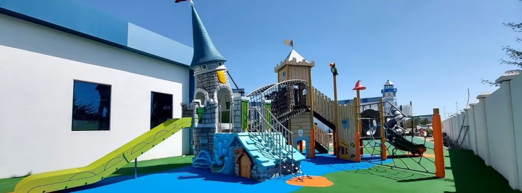 Outdoor castle-themed playground with towers, tube slides, and climbing nets on blue and green safety surfacing